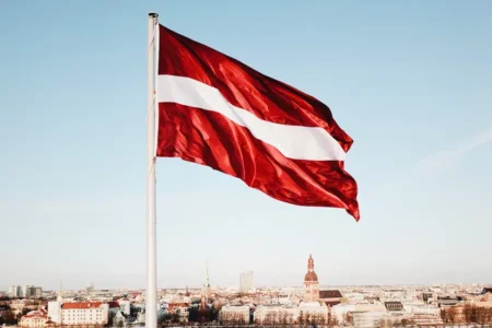 Langgar Aturan Bahasa dan Izin Tinggal, Latvia Perintahkan 841 Warga Rusia Tinggalkan Negara Bendera Latvia berkibar dengan latar belakang kota Riga (foto: Kaspars Upmanis, unsplash)